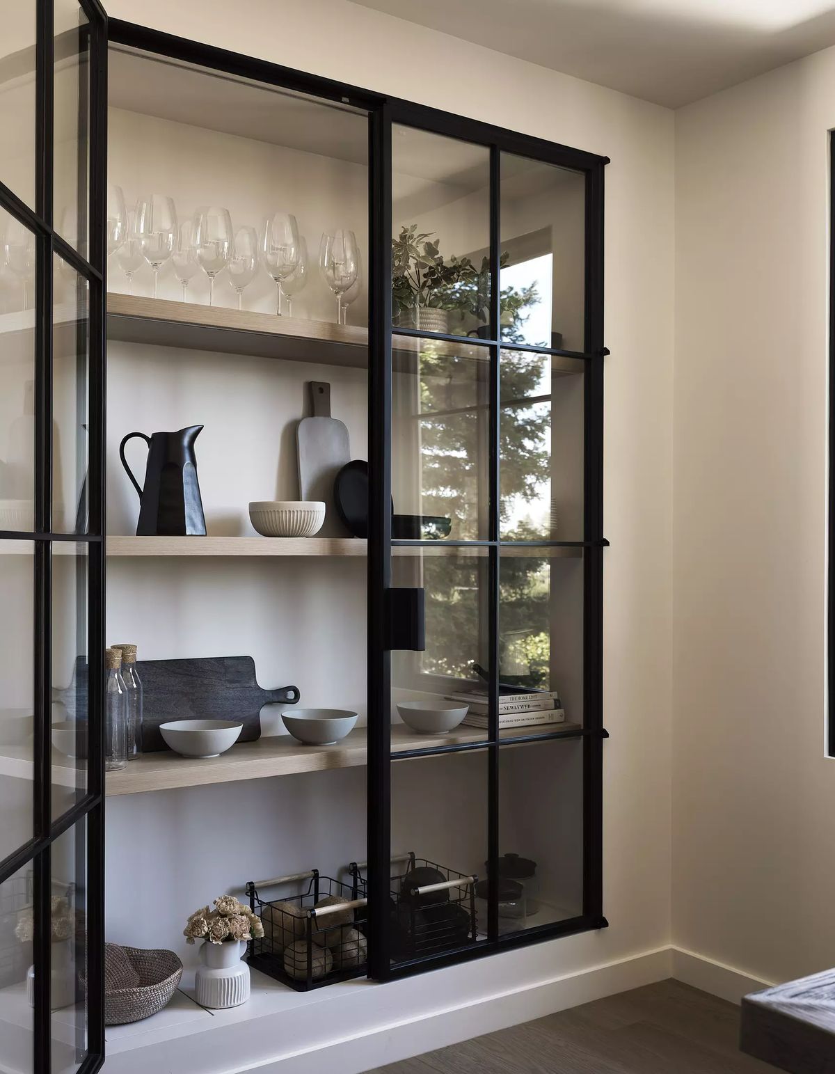 Display cabinet with black frame, glass doors, shelves with glassware, pitcher, and decorative plates.
