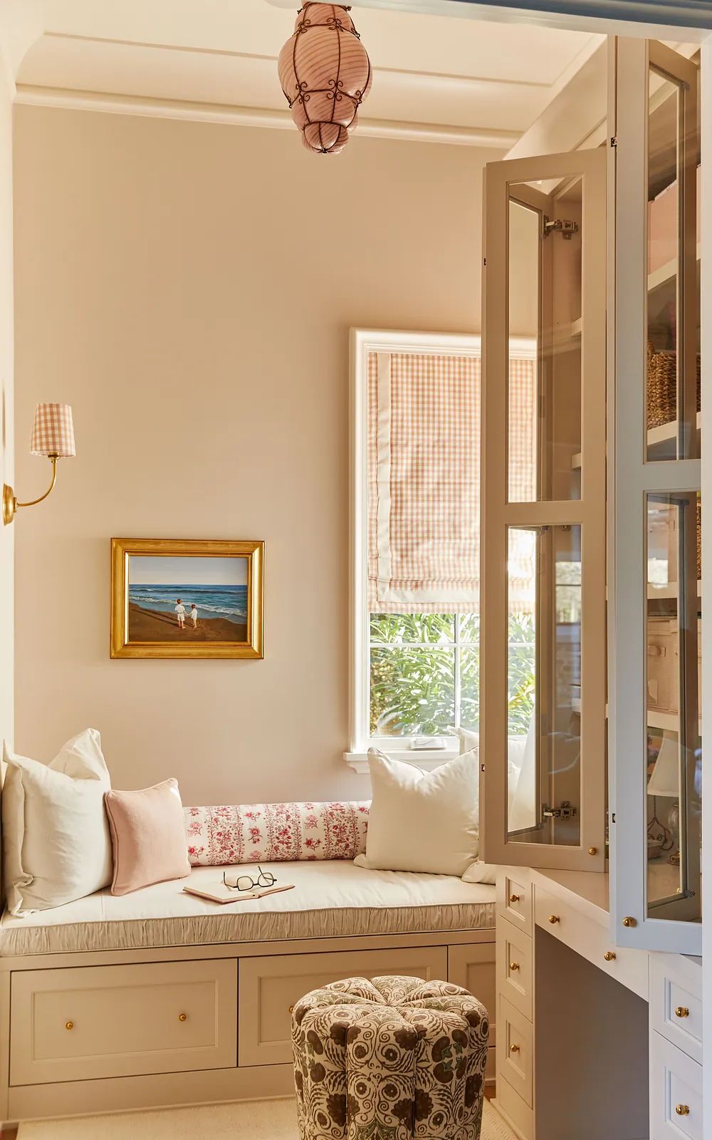 Nook with built-in bench, cushions, stool, painting, cabinetry, and window with checkered shade