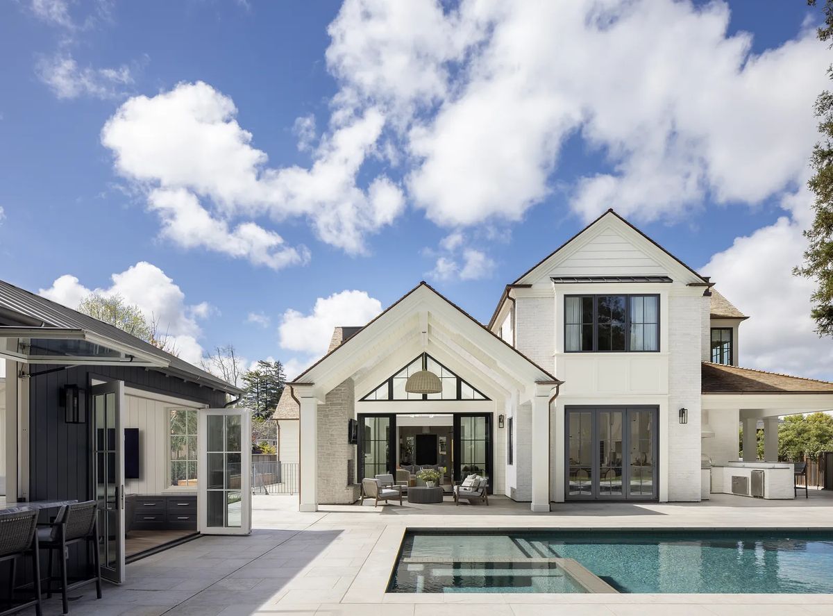 Exterior view of a house with a pool, patio, outdoor seating, and greenery.