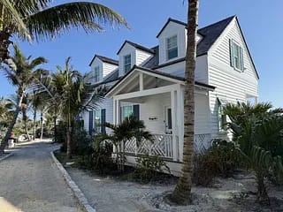 Two-story white house with gabled roofs, green shutters, and palm trees in front.
