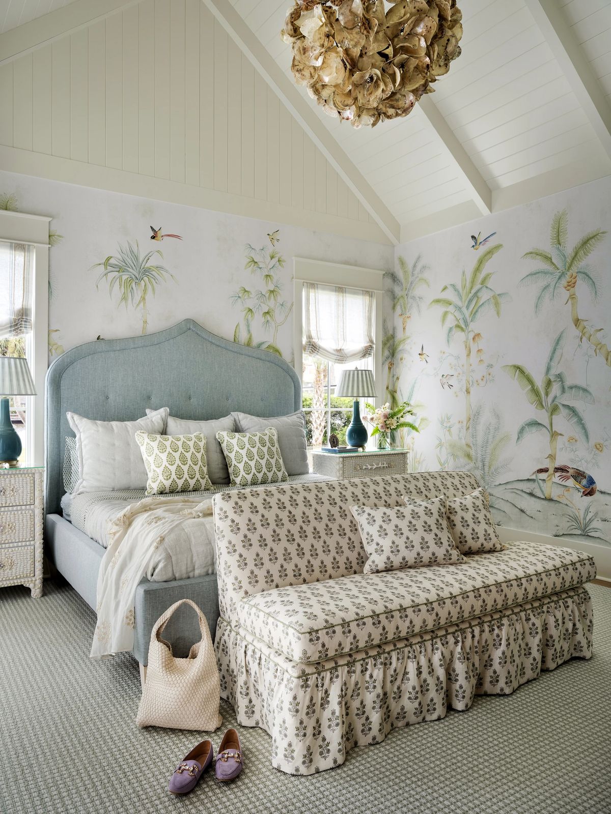 Bedroom with light blue headboard, floral sofa, bedside tables with lamps, and tropical wallpaper.