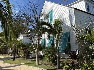 Exterior view of a white house with turquoise shutters, palm trees, and a stone pathway