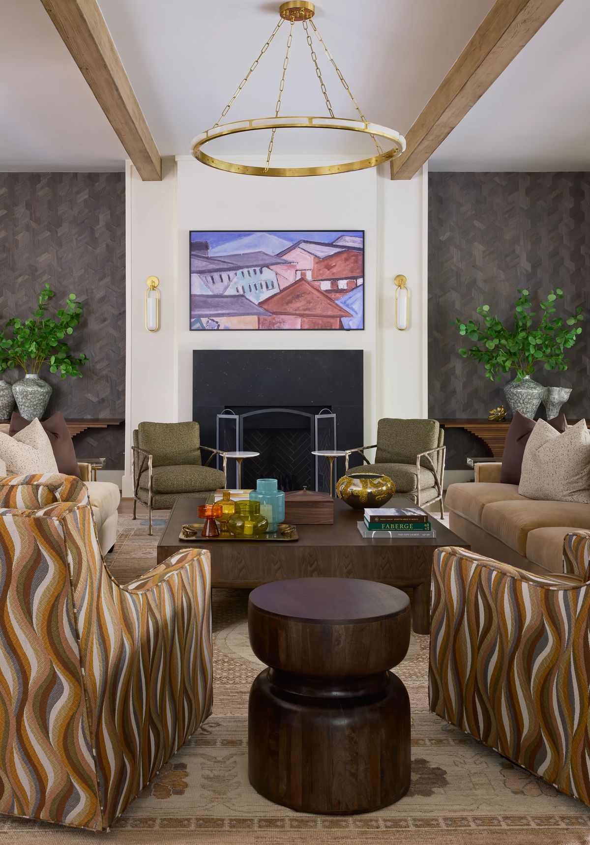 Living room with patterned armchairs, beige sofa, coffee table, artwork, plants, and black fireplace.