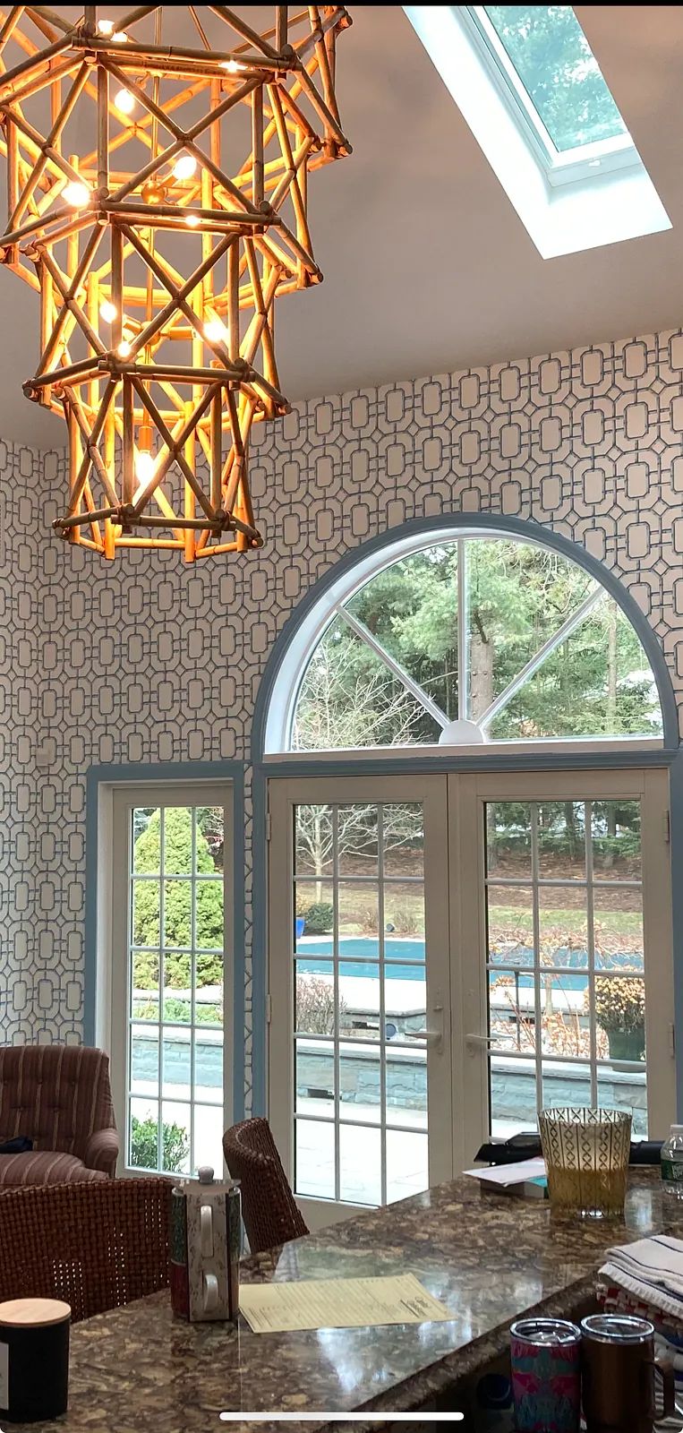 Kitchen with granite countertop, bar stools, glass doors, large windows, patterned wallpaper, and bamboo chandelier.