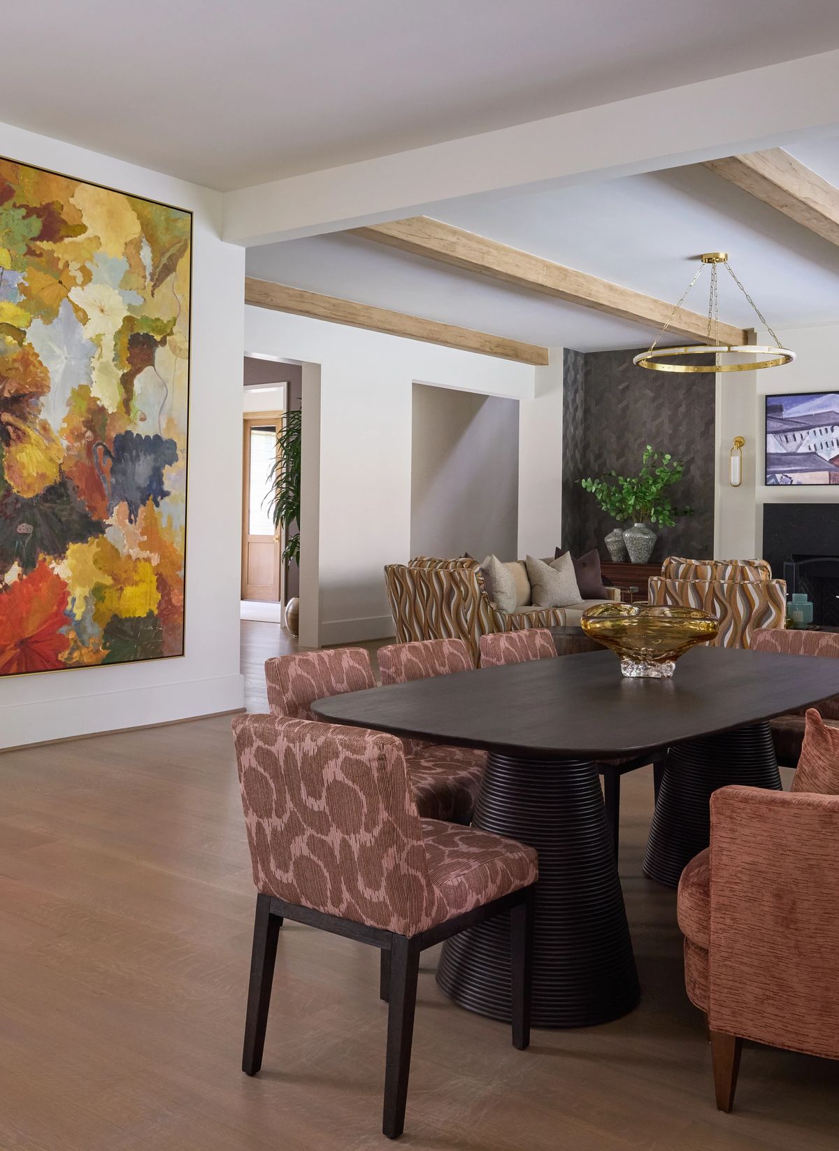 Dining room with round black table, patterned chairs, abstract art, beige sofa, and wood beam ceiling.