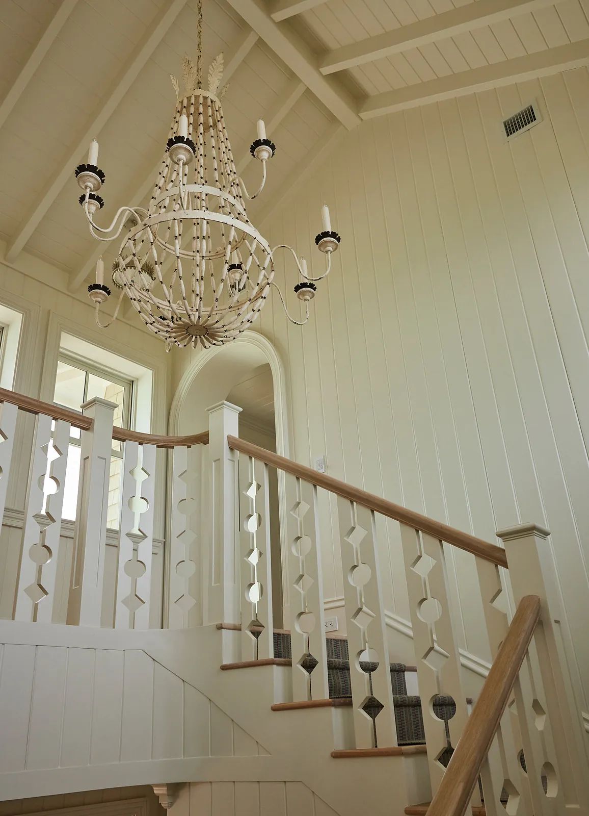 Hallway with wooden staircase, whitewashed walls, large chandelier, and circular motif banisters.
