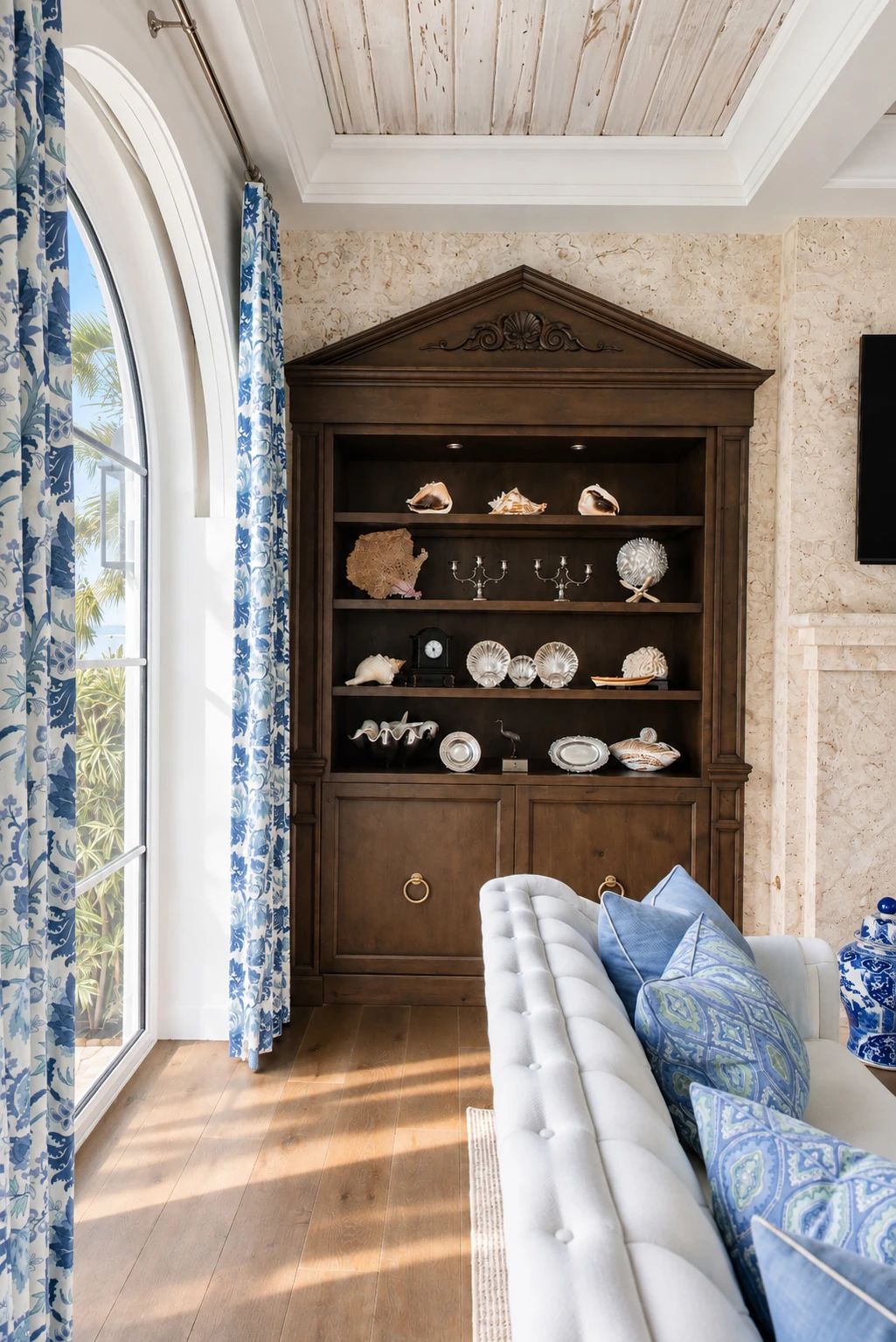 Living room with white sofa, blue and green pillows, dark cabinet, and large arched windows with blue curtains.