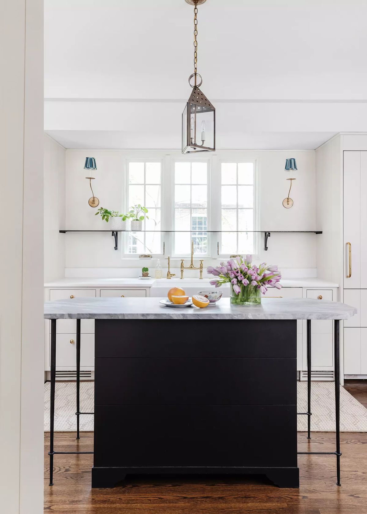 Kitchen with central black island, marble top, white cabinetry, large windows, and a vase of flowers.