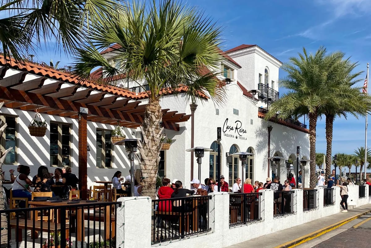 Exterior of restaurant with white stucco, red tile roof, outdoor seating, and palm trees.