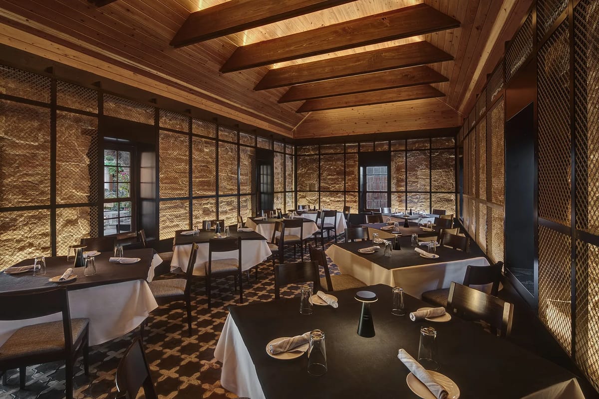 Dining room with round tables, white tablecloths, black chairs, stone walls, and wooden beams.