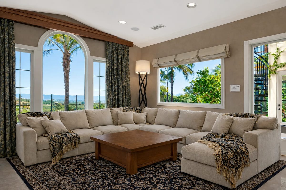 Living room with large sectional sofa, wood coffee table, area rug, curtains, large windows, and staircase.