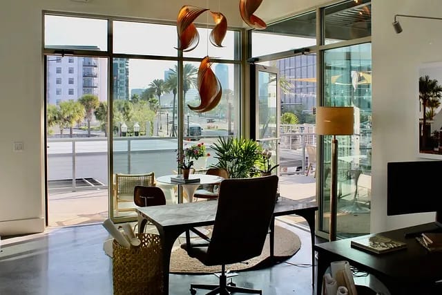 Office with large desk, ergonomic chair, round rug, potted plants, and glass doors leading outside.