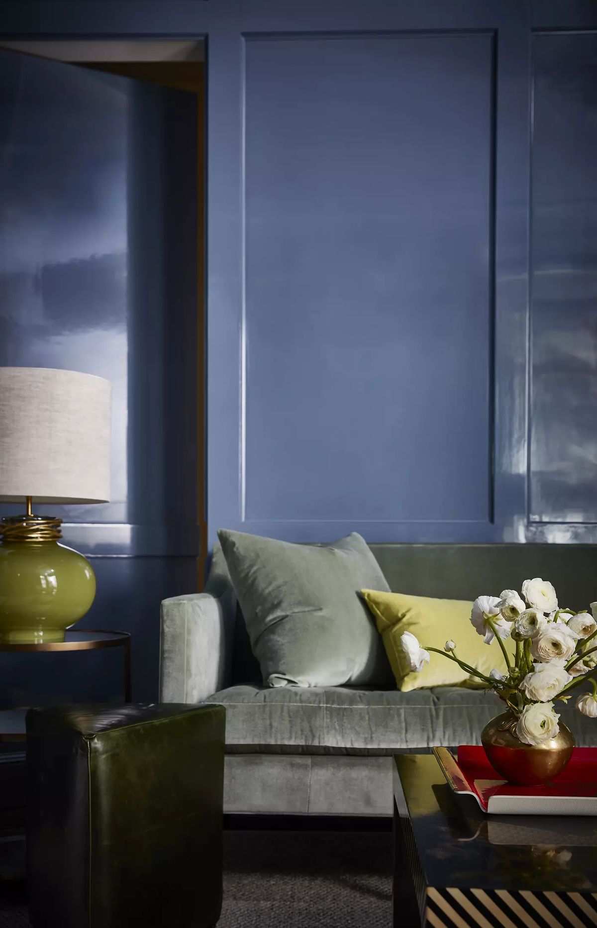 Living room with green sofa, yellow pillow, side table with lamp, floral arrangement, and rectangular coffee table.