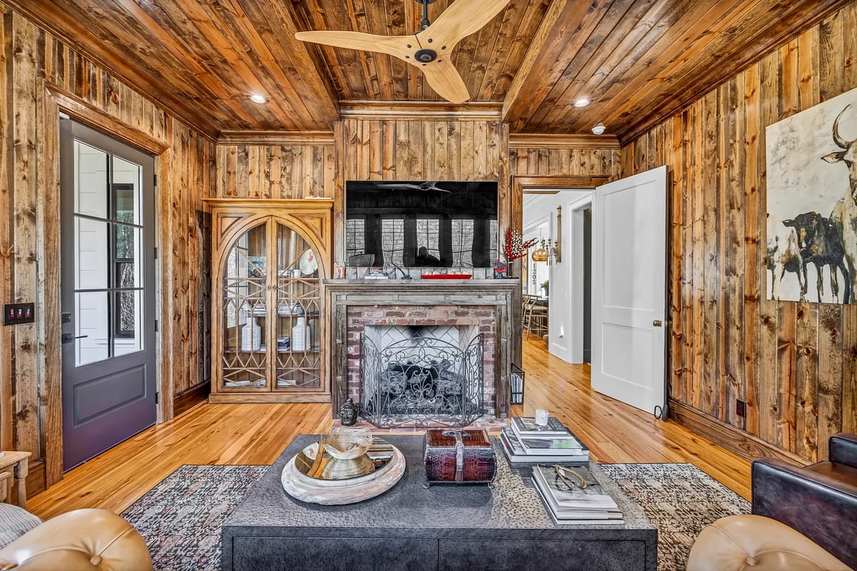 Living room with black coffee table, brown sofa, brick fireplace, wood-paneled walls, and ceiling fan.