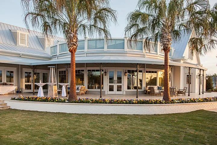 Exterior rear view of single-story building with terrace, sliding doors, palm trees, and colorful flowerbed