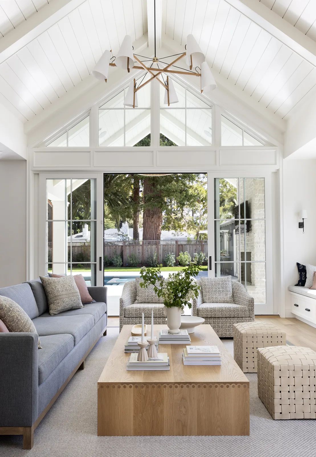 Living room with gray sofa, wooden coffee table, patterned ottomans, and vaulted ceiling with beams.