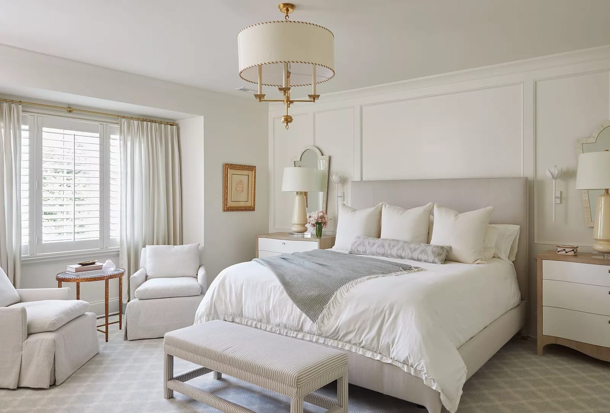 Bedroom with king-sized bed, nightstands, lamps, armchair, bench, and chandelier.