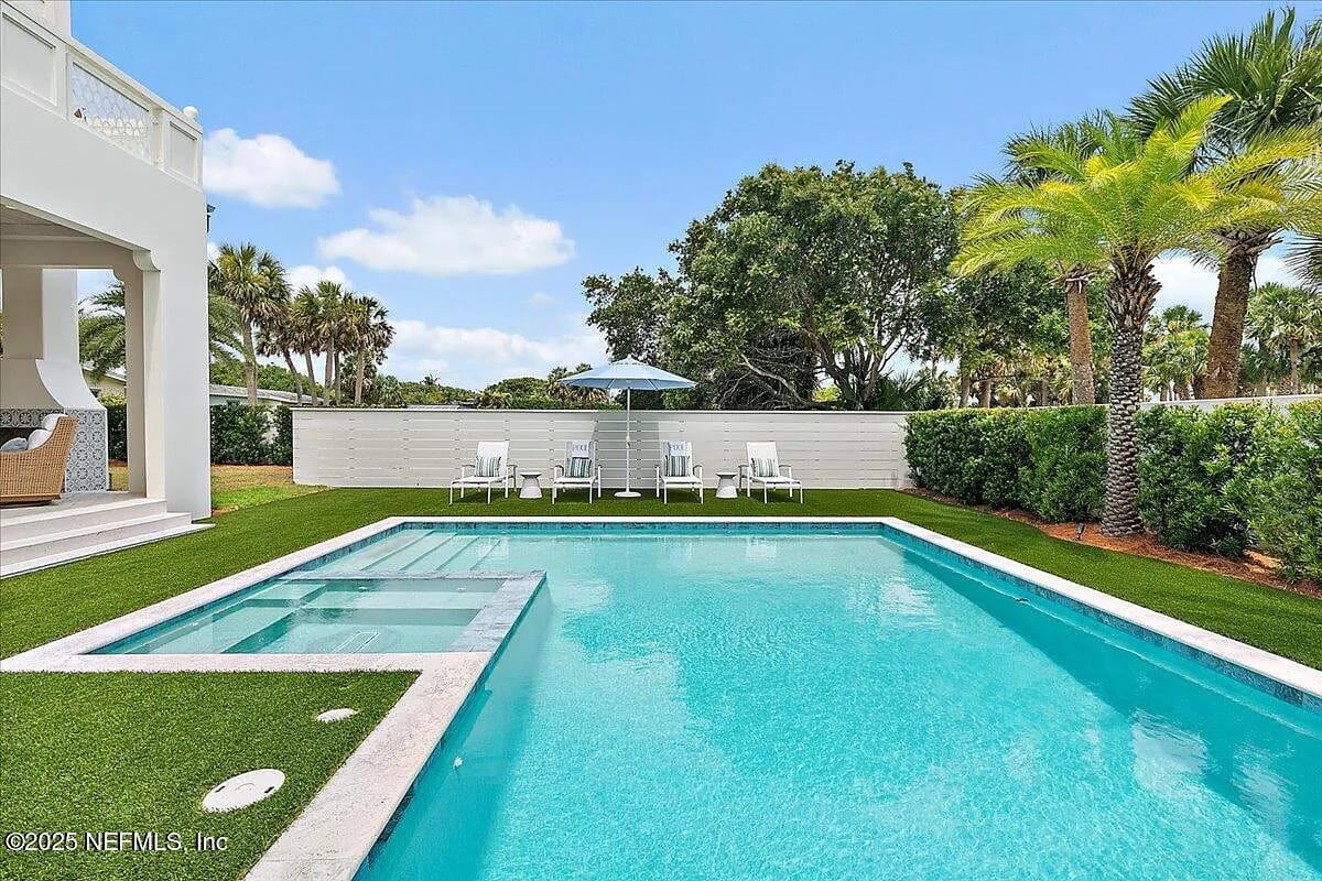 Exterior rear space with swimming pool, marble decking, lounge chairs, umbrella, and palm trees