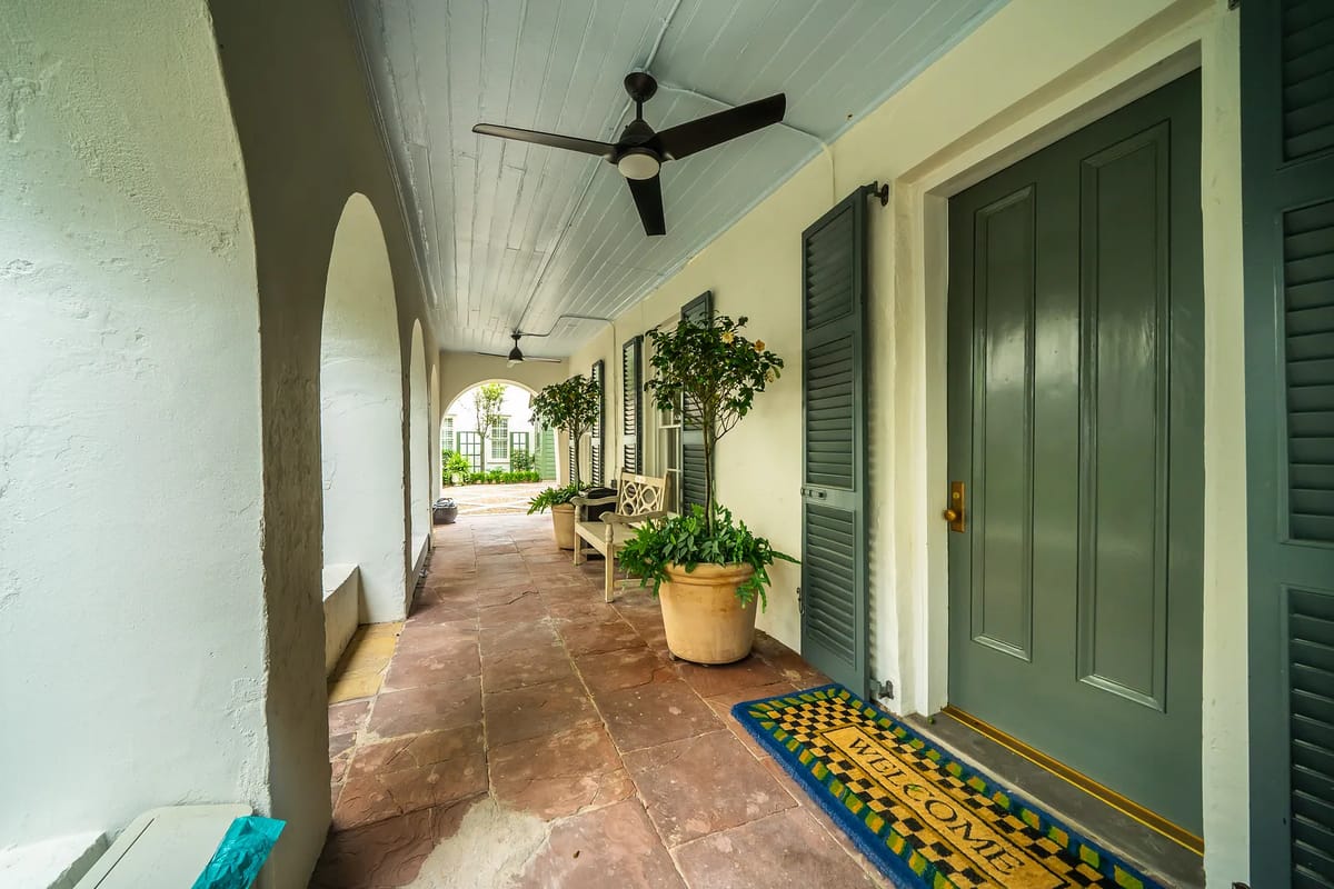 Foyer with stone floor, gray front door, green shutters, wooden bench, and potted plant.