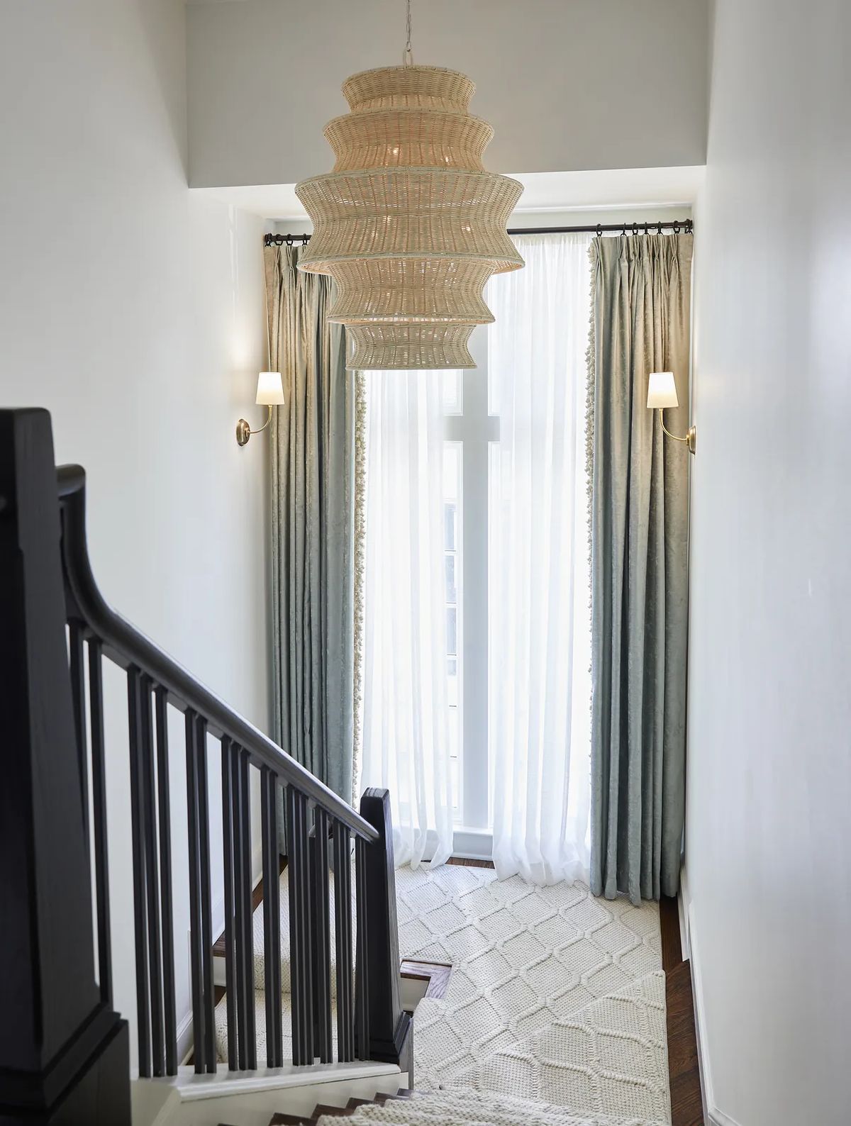 Hallway with staircase, woven pendant light, gray curtains, and patterned rug on wooden floor