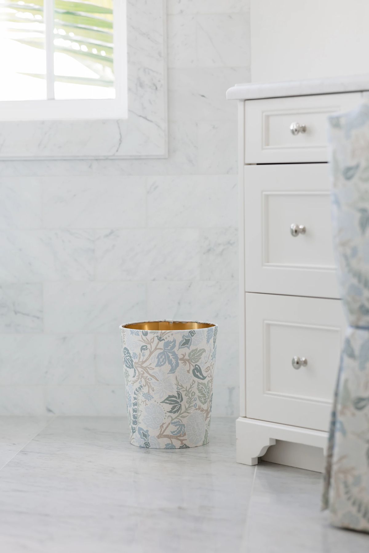Bathroom with white marble floor, decorative wastebasket, and cabinet with drawers.