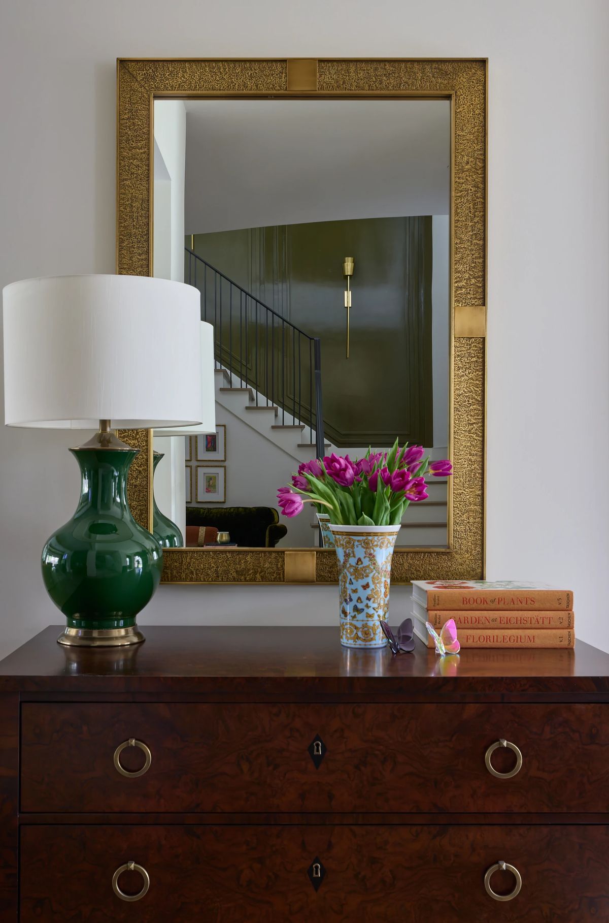 Entry table with green lamp, mirror, vase of tulips, and background staircase.