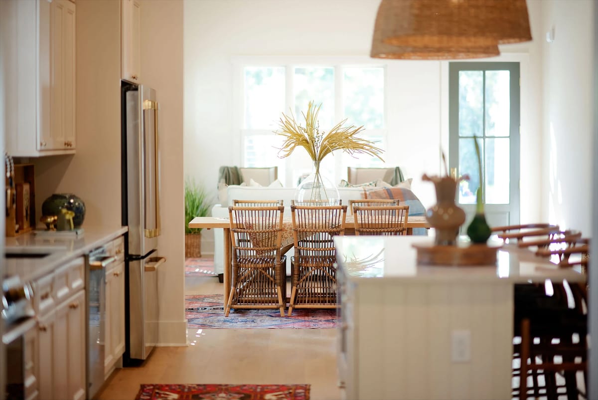 Kitchen with white cabinets, marble countertop, dining table, rattan chairs, and natural light from windows.