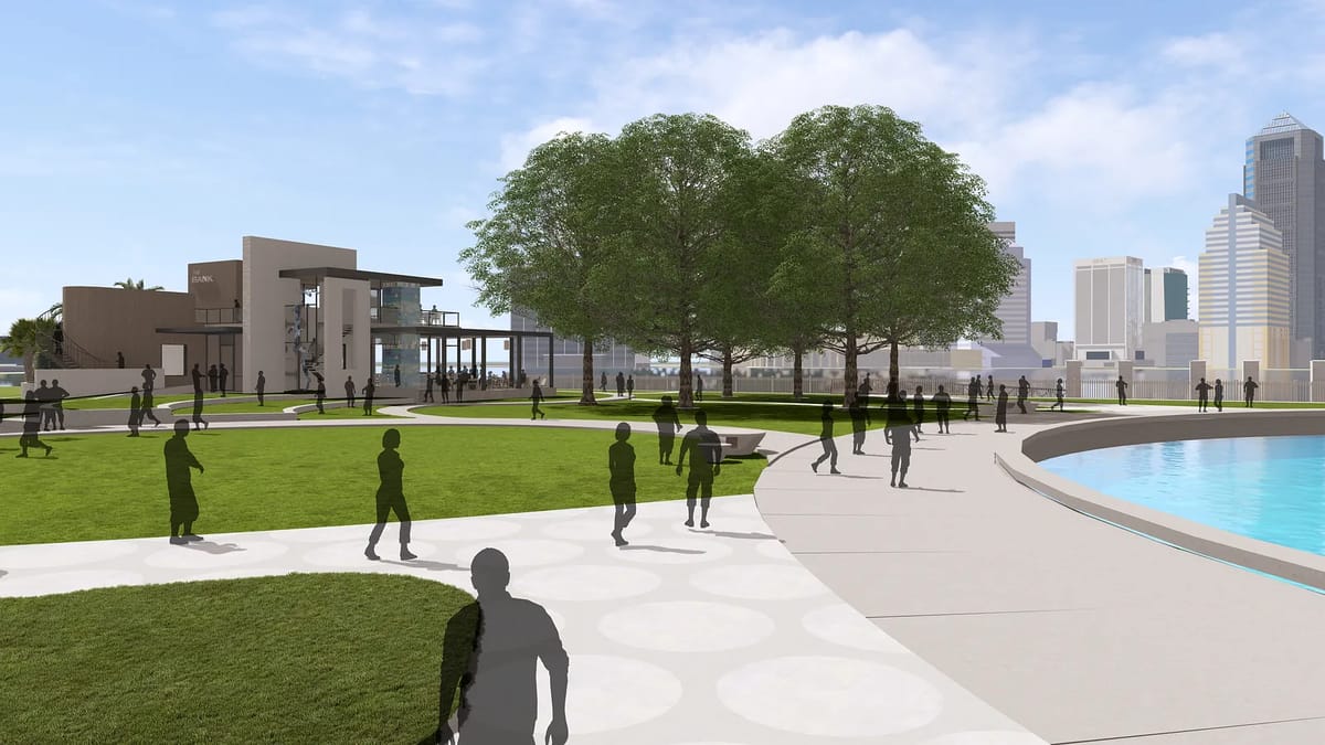 Outdoor park with grassy area, walking paths, trees, water, and a background building.