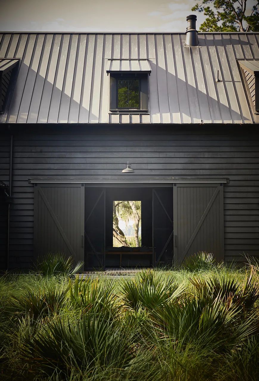 Exterior front of a barn-style building with metal roof, wooden siding, large double doors, and landscaped area.