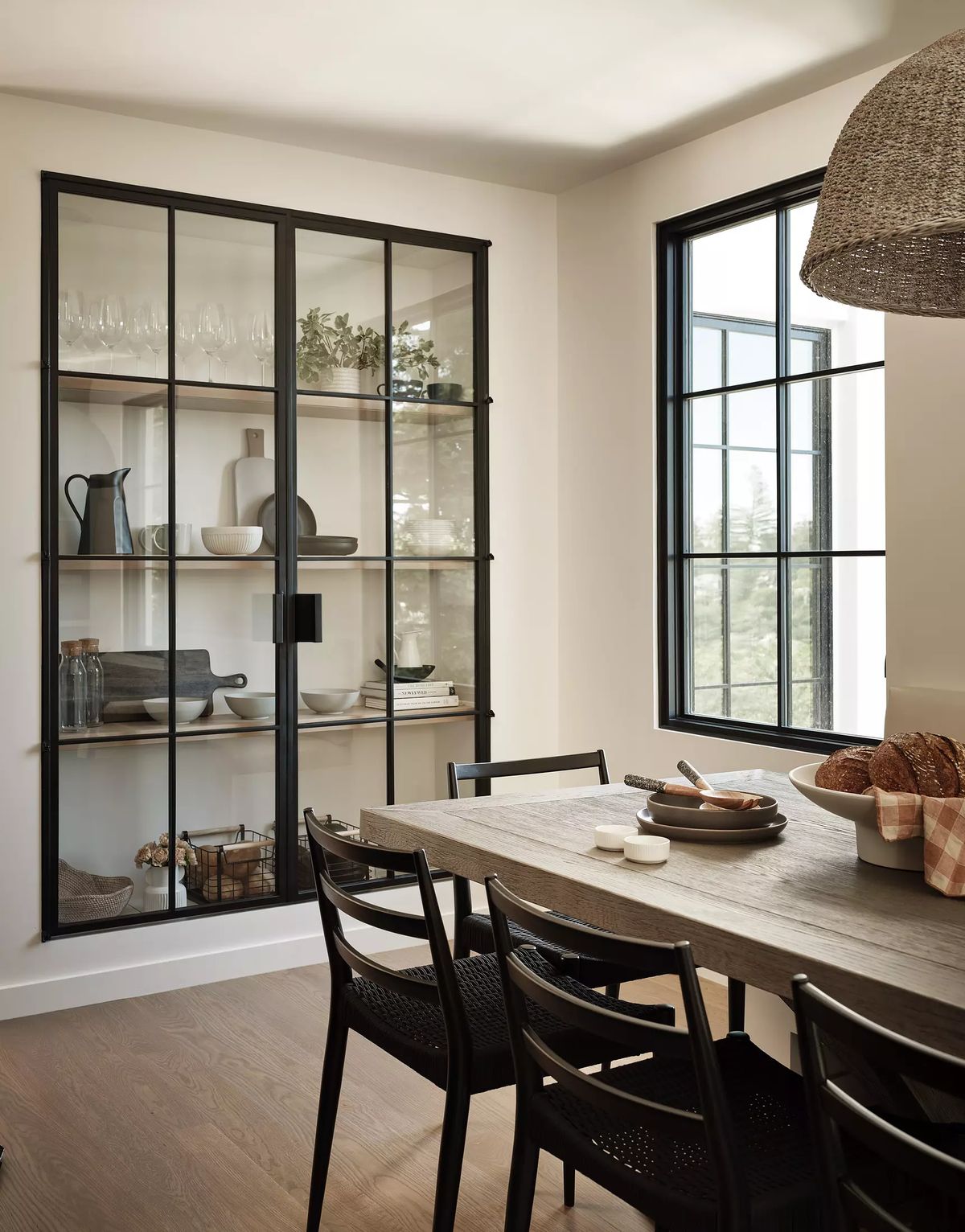 Dining room with wooden table, black chairs, glass cabinet, large window, and pendant light
