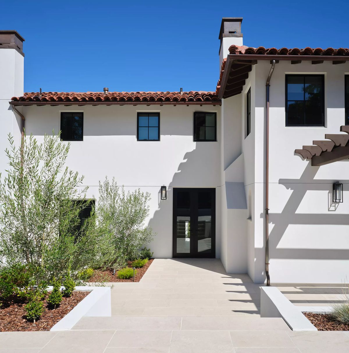 Exterior front with white stucco, terracotta roof, symmetrical windows, plants, and a stone pathway.
