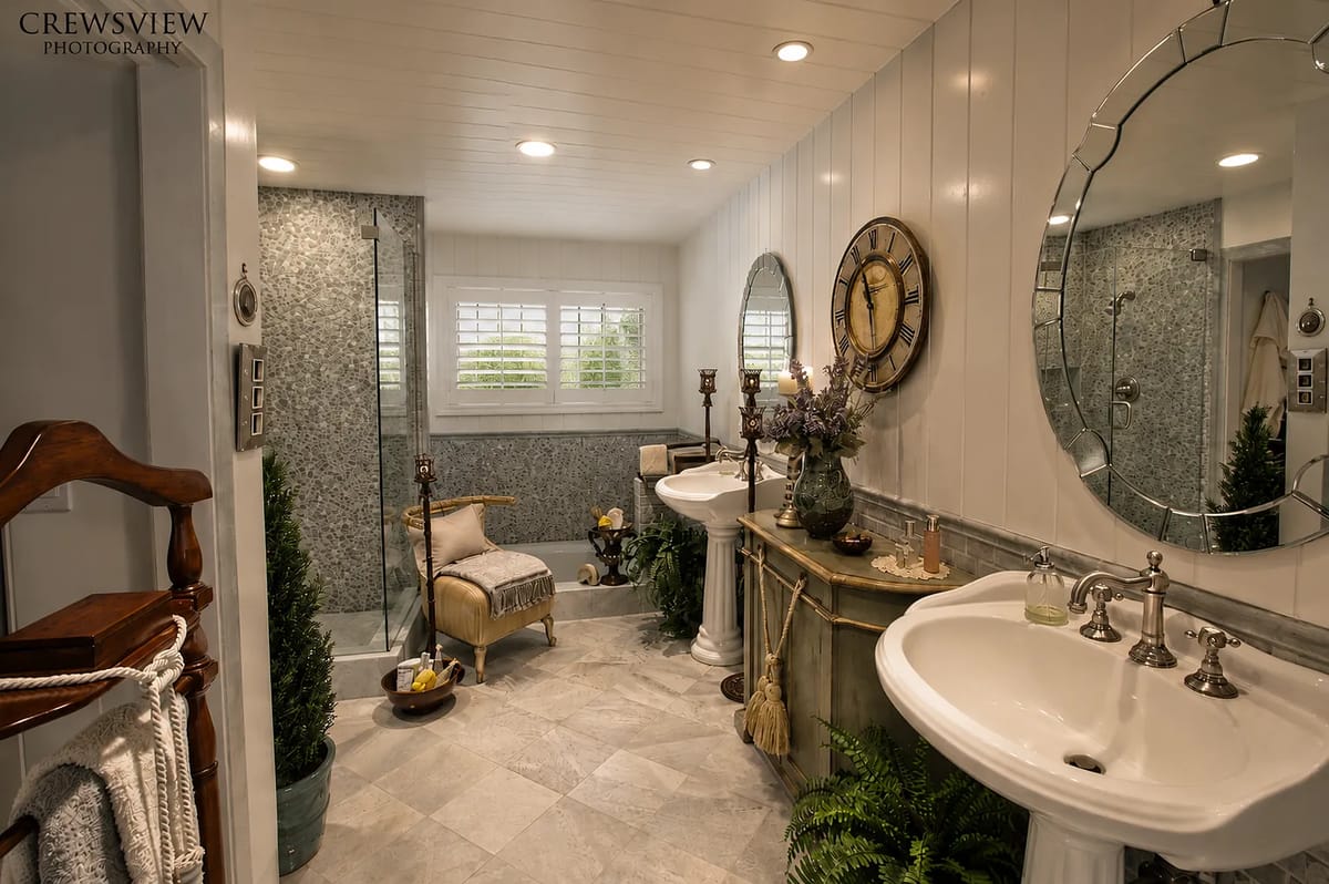 Bathroom with two pedestal sinks, decorative mirrors, walk-in shower, and stone tile flooring.