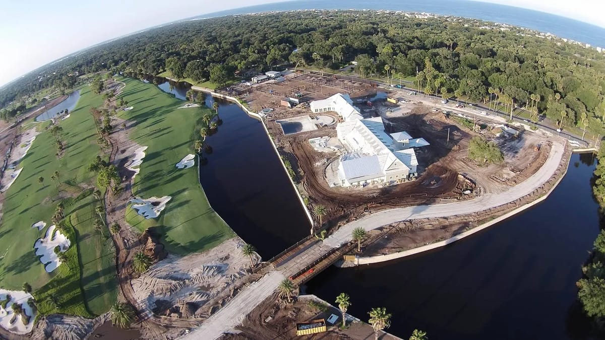 Aerial view of a construction site with a building, water, golf course, and earth-moving equipment.