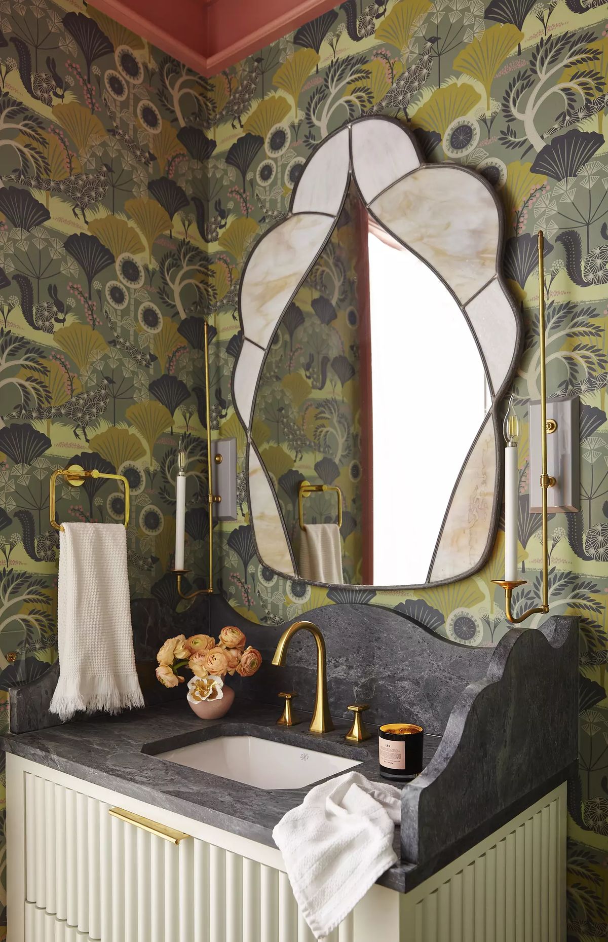 Bathroom with marble sink, gold faucets, floral wallpaper, decorative mirror, and towel holders.