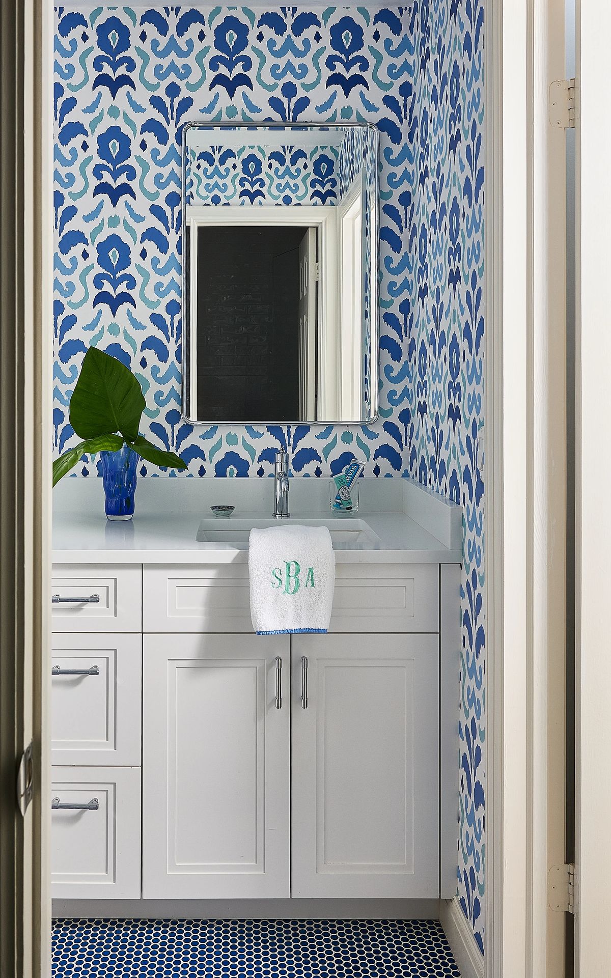 Bathroom with white vanity, sink, wall mirror, patterned blue wallpaper, and blue tile flooring.