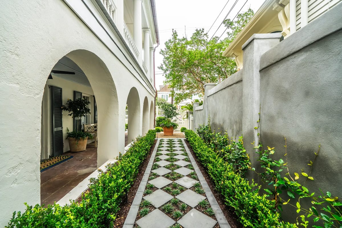 Garden pathway with boxwood hedges, pavers, archways, and a potted plant.