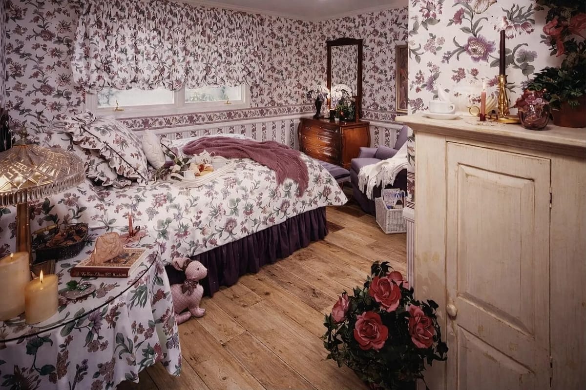 Bedroom with floral bedspread, wooden dresser, mirror, nightstand, stuffed animal, and decorative candles.
