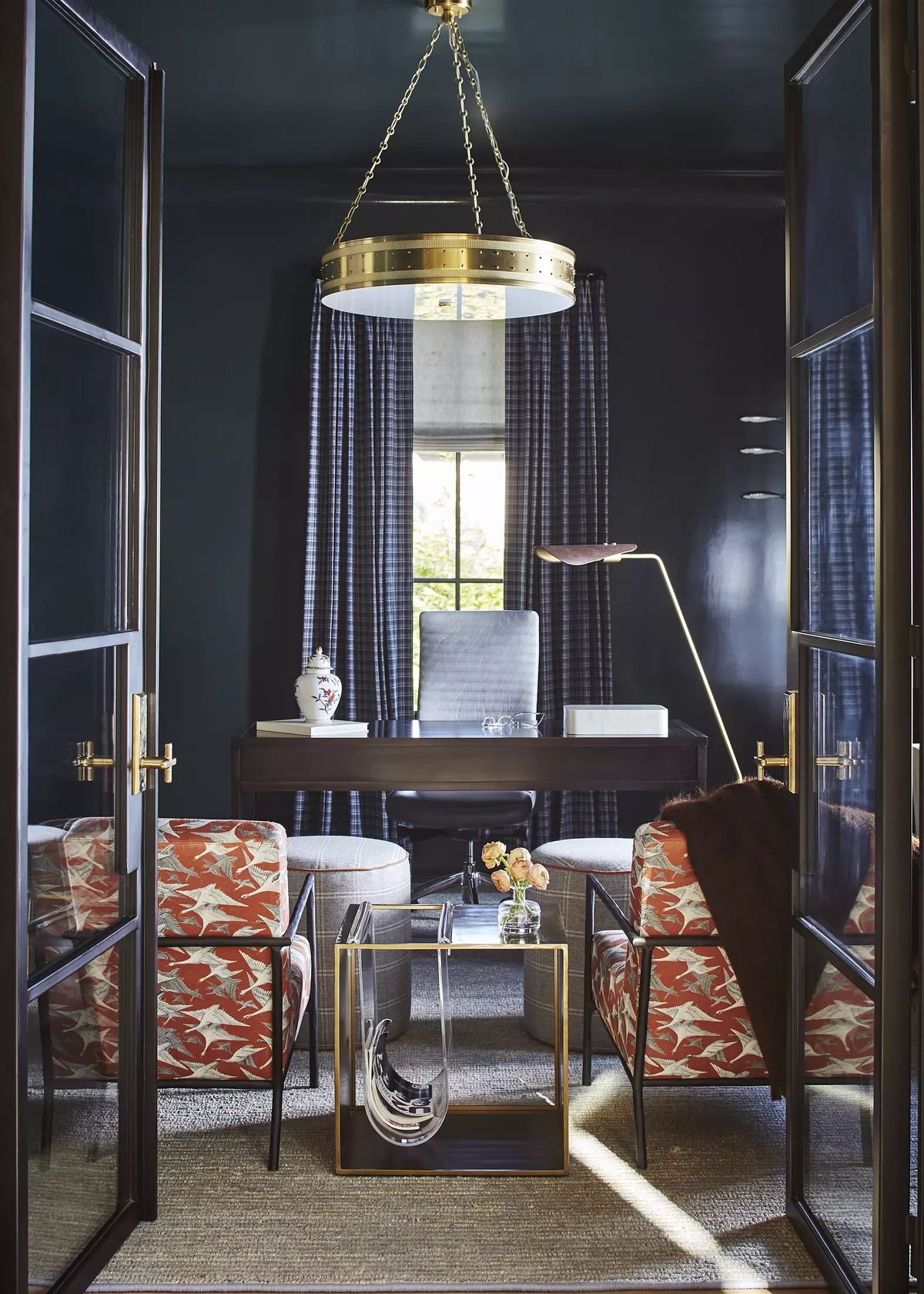 Office with dark blue ceiling, floral armchairs, glass coffee table, wooden desk, and floor-to-ceiling windows.