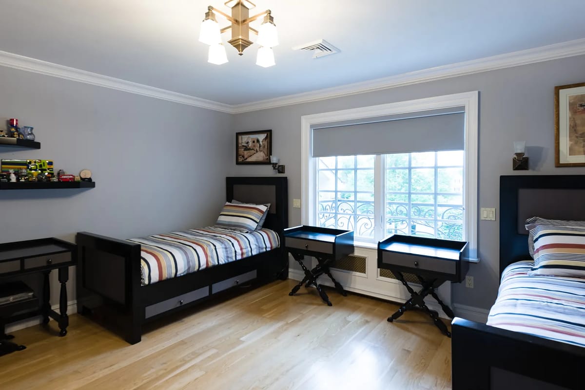 Bedroom with twin beds, black nightstands, large window with gray blind, and wall shelf with toys
