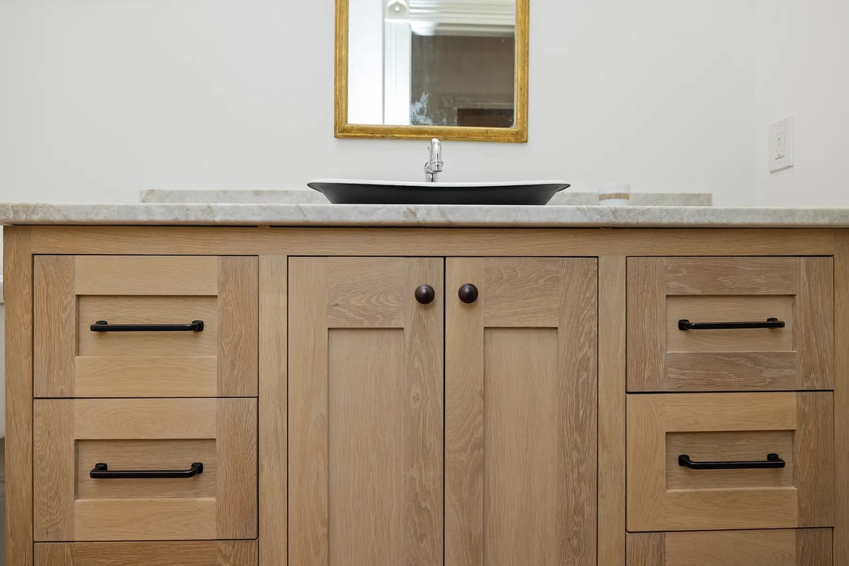 Bathroom with wooden vanity, marble countertop, black vessel sink, and wall-mounted mirror.