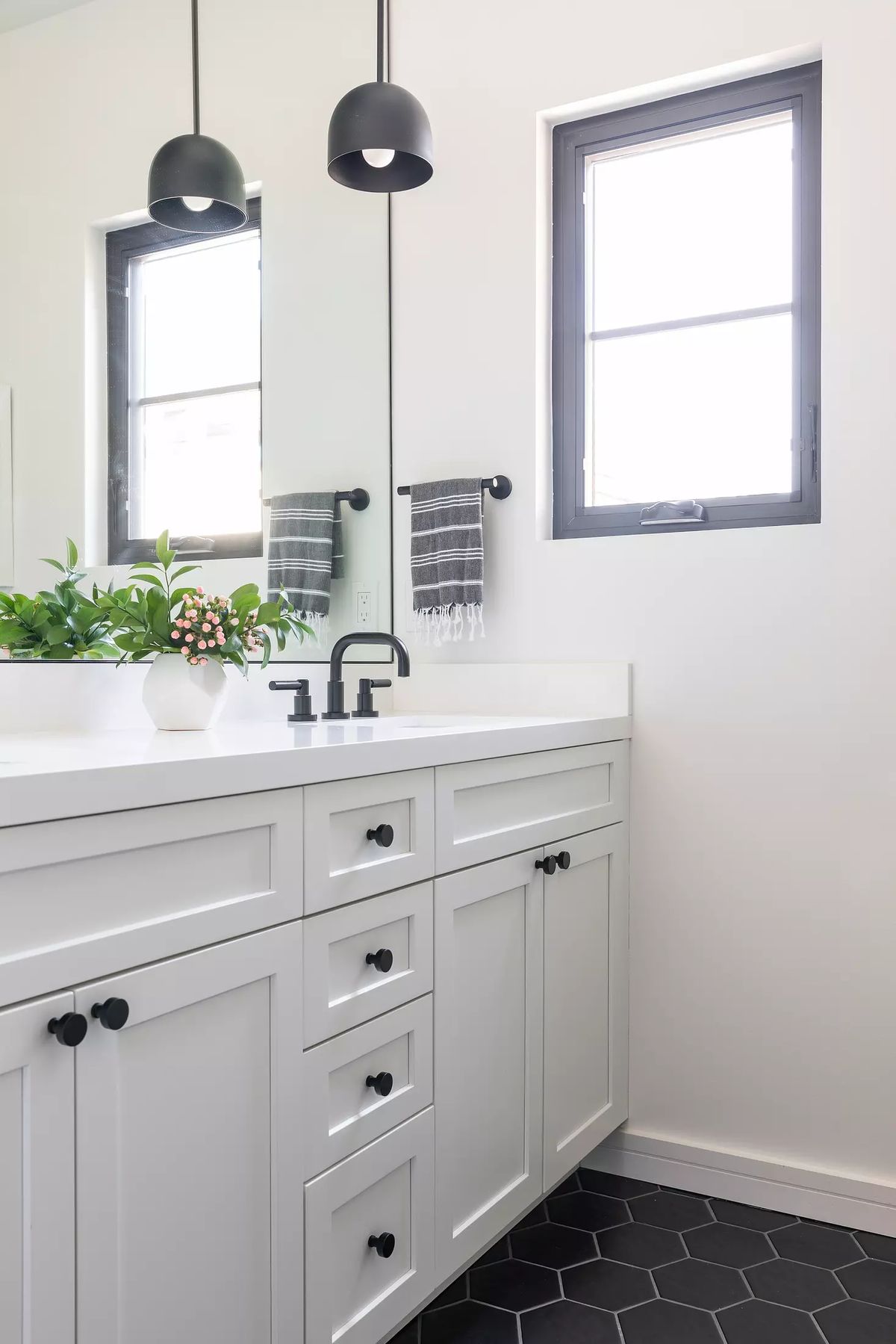 Bathroom with white vanity, black hardware, sink, mirror, pendant lights, hexagonal tiles, and a potted plant.