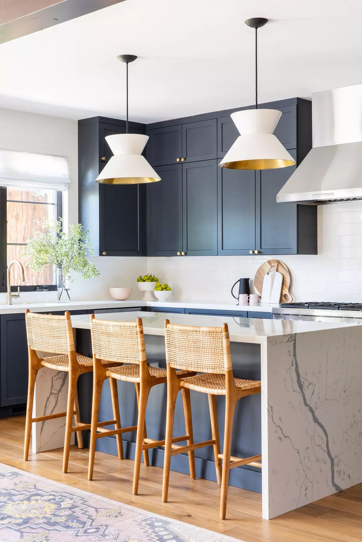 Kitchen with marble island, wooden barstools, dark blue cabinetry, and stainless steel range hood.