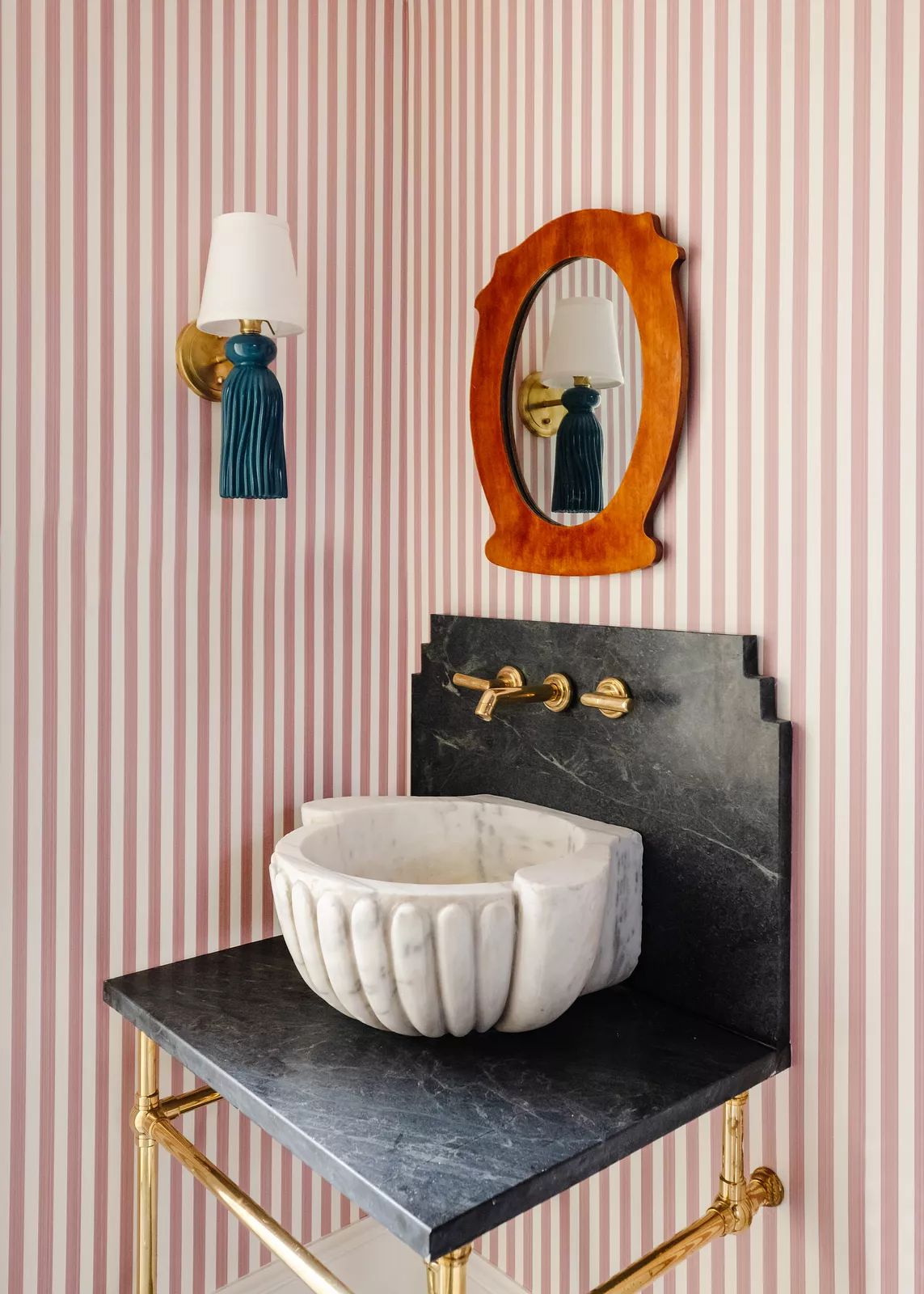 Powder room with striped wallpaper, marble sink, gold faucet, and wooden-framed mirror