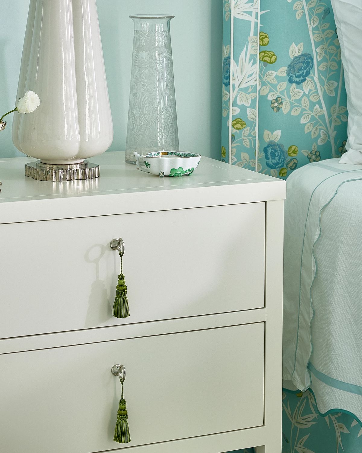 Bedroom with white nightstand, decorative vase, floral headboard, and light blue walls.
