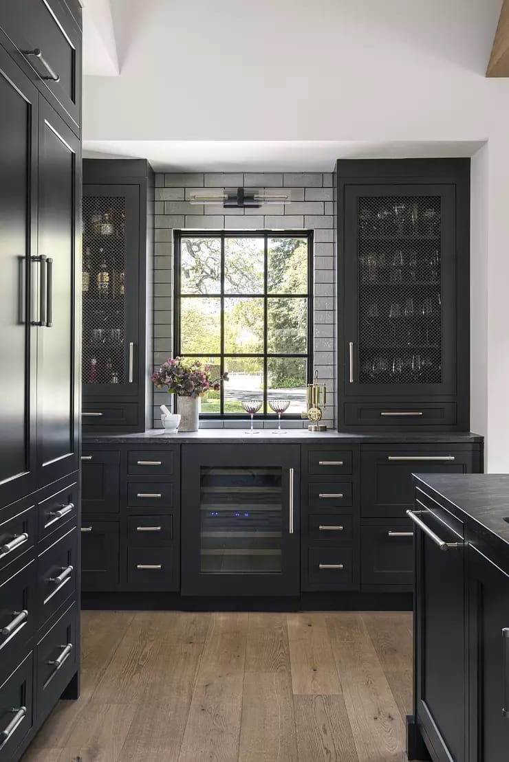 Kitchen with dark cabinetry, wine refrigerator, large window, and wood flooring.