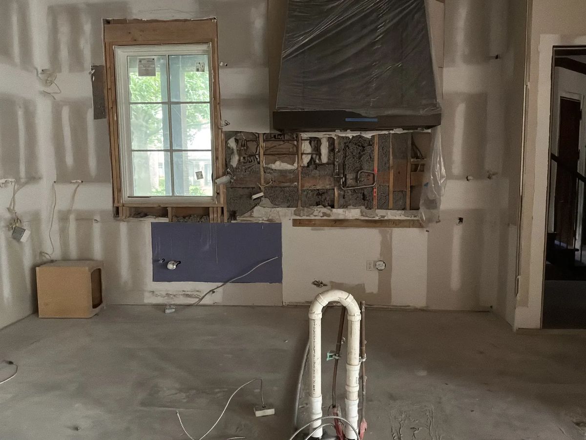 Under-construction kitchen space with exposed walls, window, plumbing, and electrical preparations.