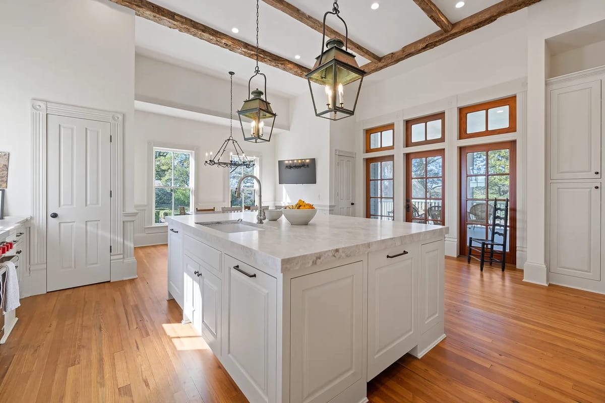 Kitchen with large marble island, white cabinetry, hardwood floor, and lantern-style lighting fixtures.