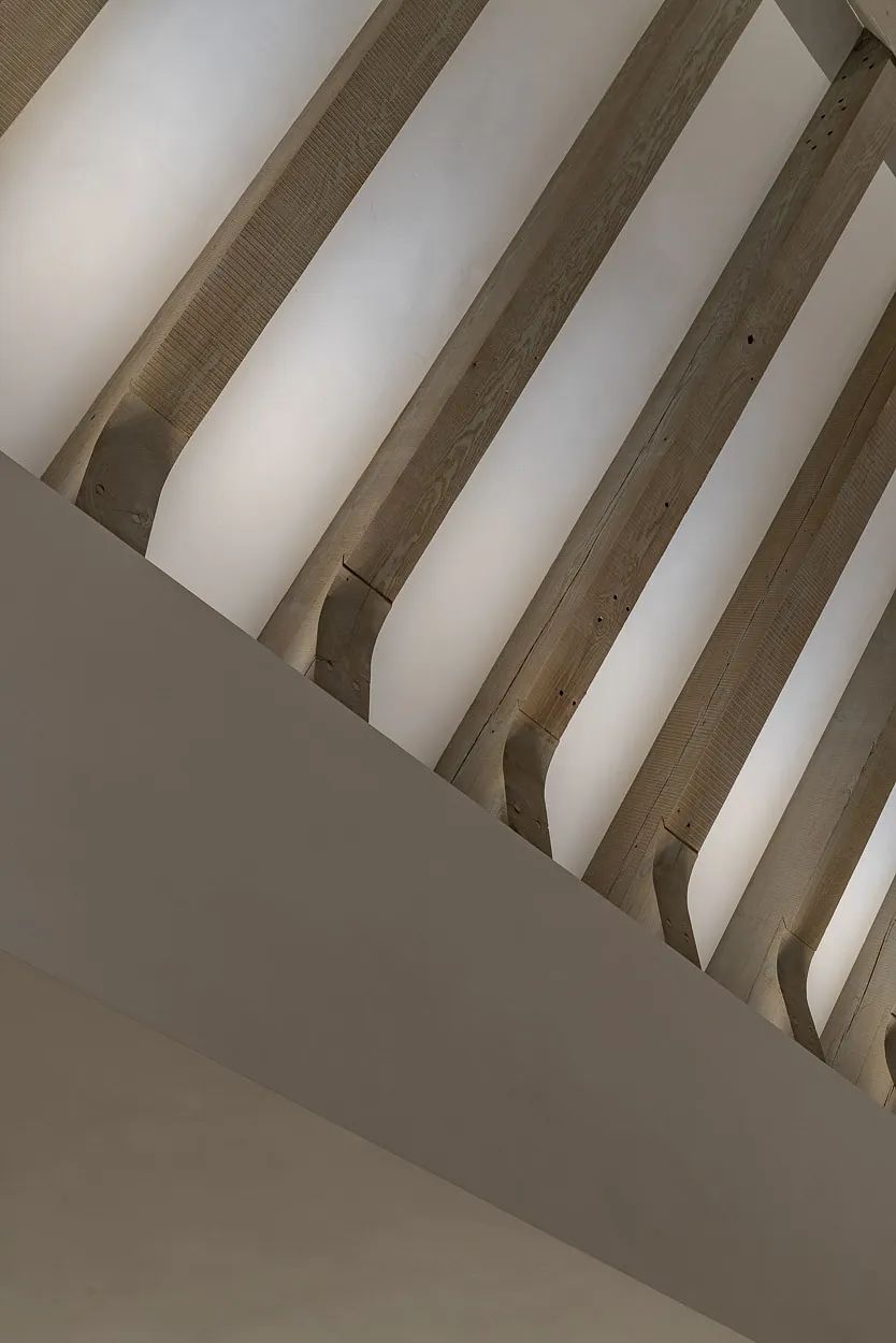 Ceiling view with exposed wooden beams in geometric pattern and smooth white ceiling.