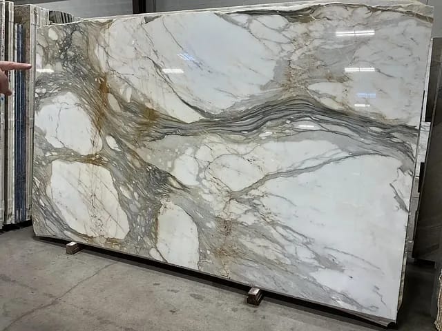 Large marble slab with white base and gray, gold veining displayed in a warehouse.