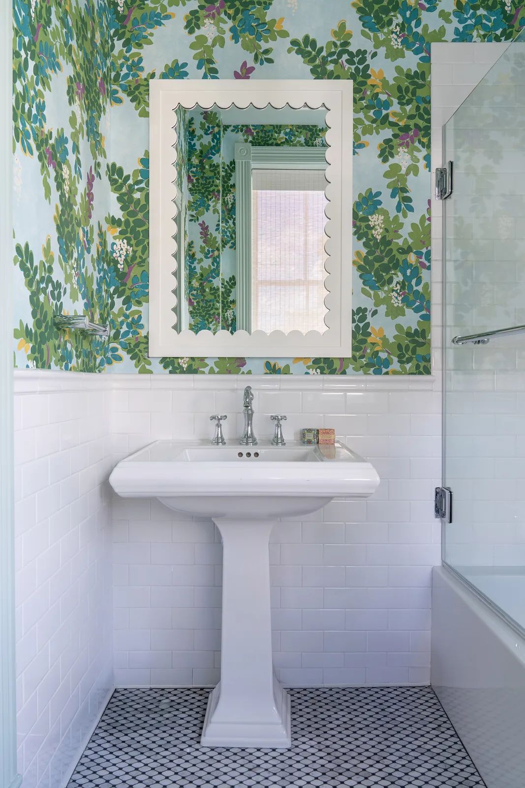 Bathroom with pedestal sink, floral wallpaper, tile wainscoting, and black and white patterned floor.